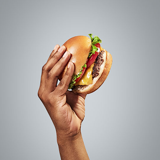 A hand holding a cheese burger