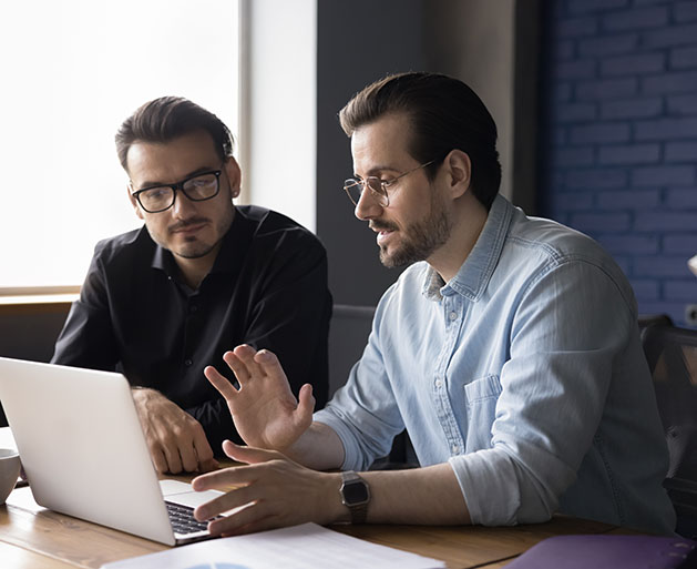 Two men at laptops discussing integrated payment processing systems